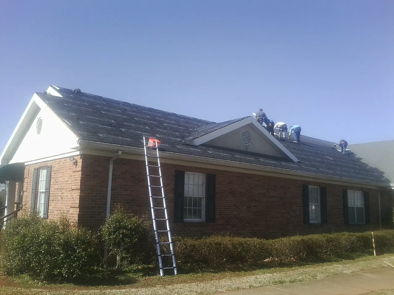Crew tearing shingles off a brick ranch roof with a ladder set — Metal Roof Repair work by our crew in Killbuck