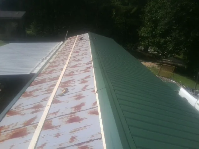 Old rusted panels beside newly installed green metal roofing — Wind Damage Roof Repair by Roofing Brothers in Killbuck