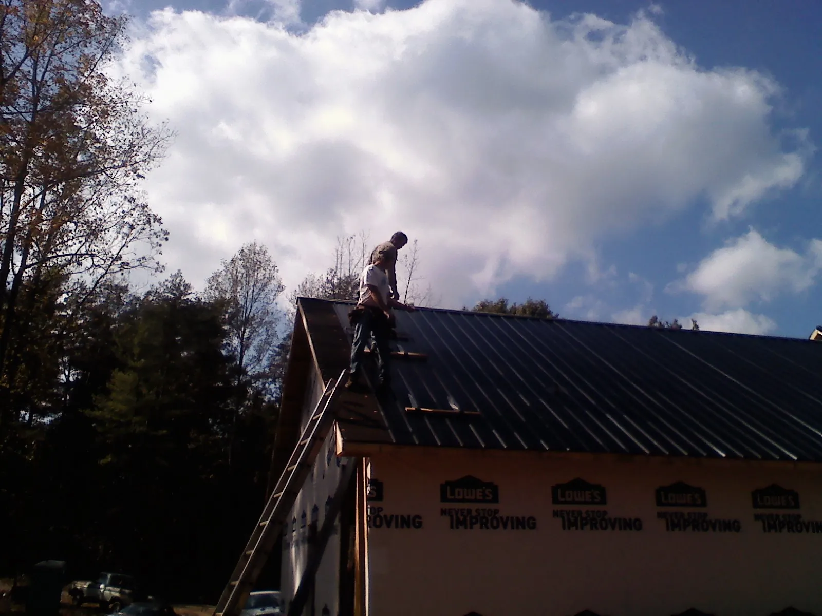 Roofer fastening dark metal panels high against a cloudy sky, from a Roof Inspection job in Killbuck