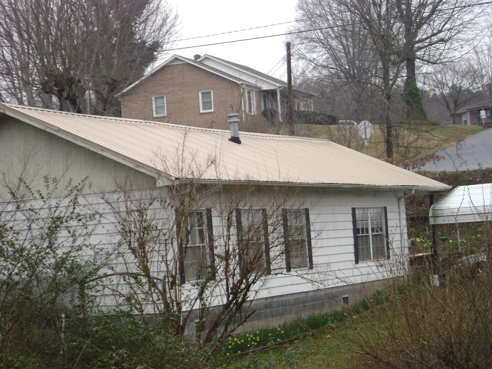 Tan metal roof on a white sided house set into a hillside — Commercial Roofing by Roofing Brothers in Killbuck