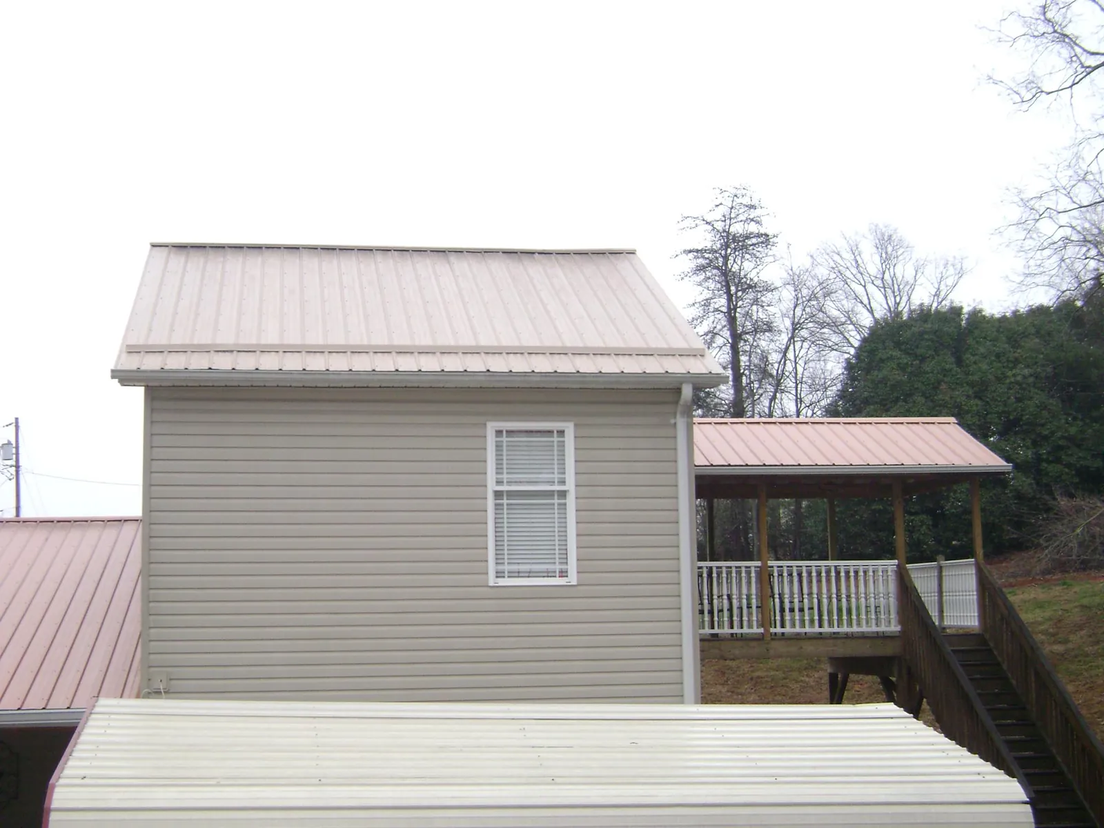 Tan metal roofs on a two story addition and attached porch, from a Roof Replacement job in Killbuck